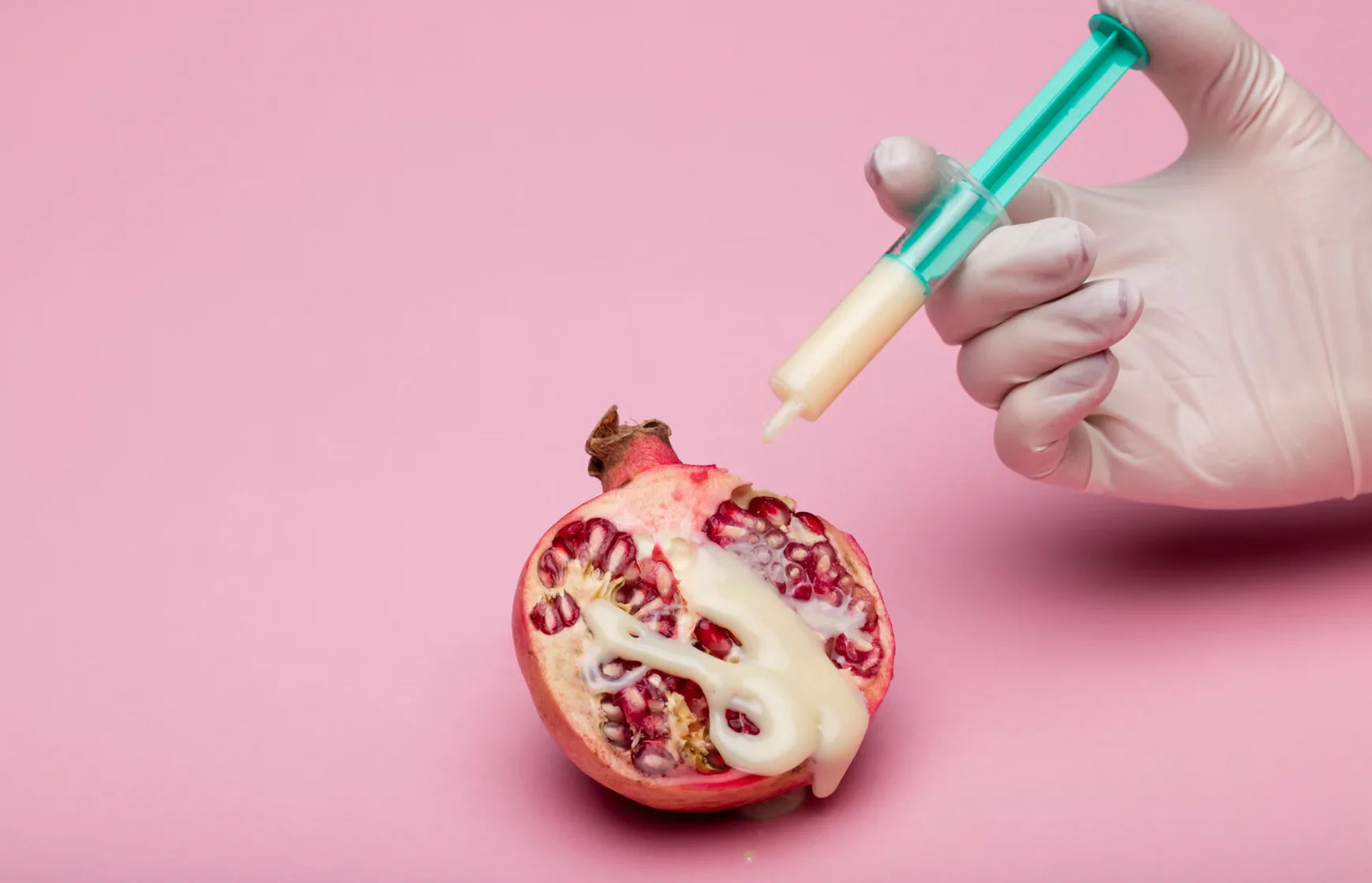 a syringe of milky liquid is ejected over a halved pomegranate